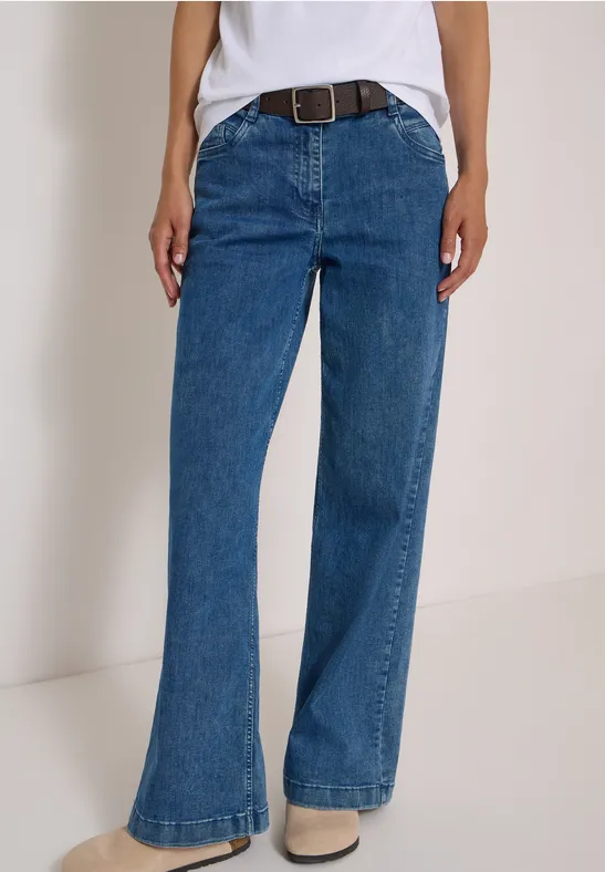 Eine Person trägt hoch sitzende, leicht ausgestellte blaue Jeans mit Gürtel.