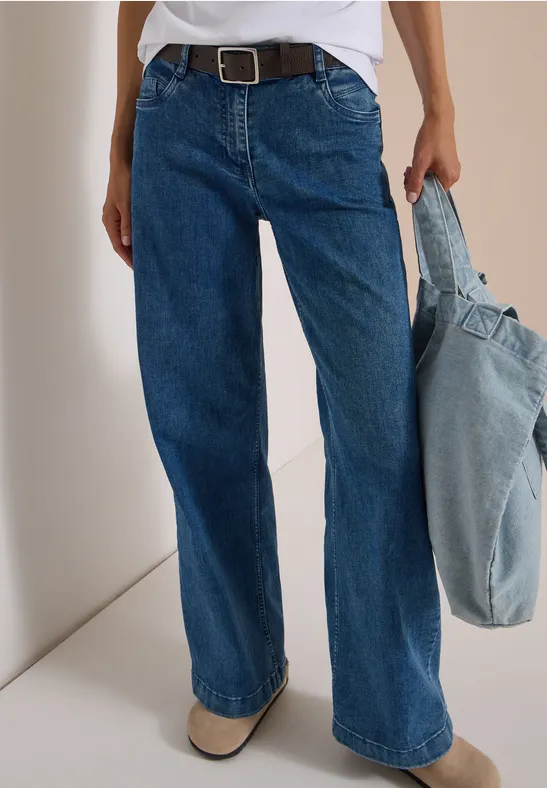 Person trägt weite blaue Jeans mit Gürtel und hält eine hellblaue Jeans-Tasche.