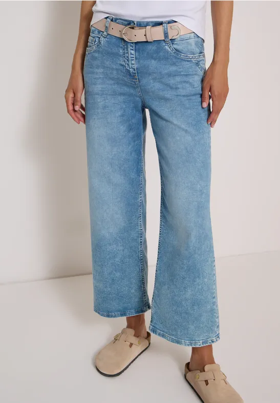 Weite, hellblaue Cropped-Jeans mit beigem Gürtel und hellbraunen Slippern.