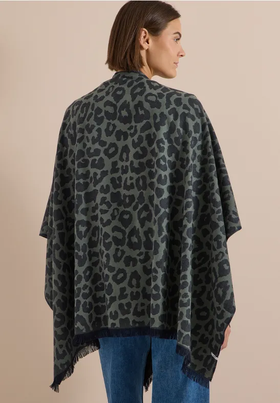 Rückansicht: Frau in olivgrünem Poncho mit schwarzem Leopardenmuster.