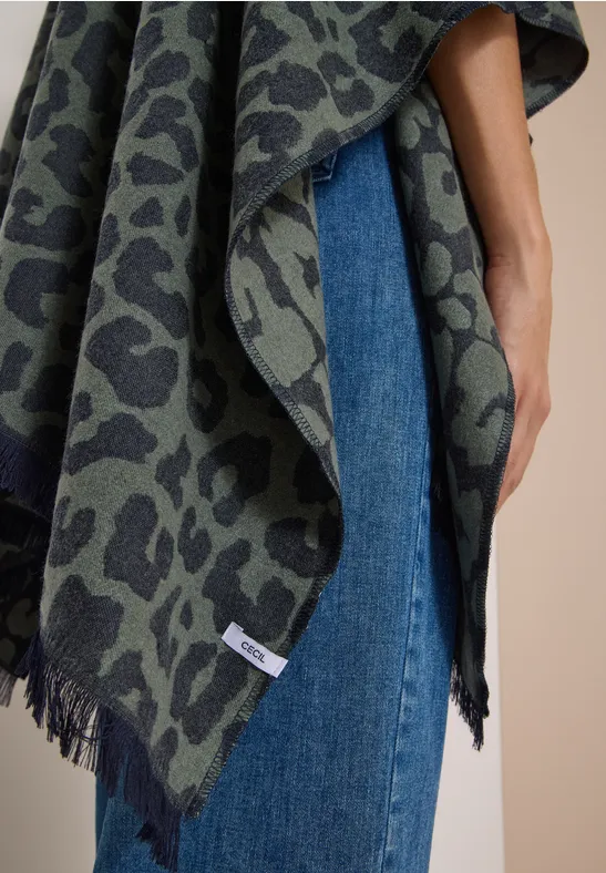 Eine Person trägt einen grün-grauen Poncho mit Leopardenmuster über blauen Jeans.