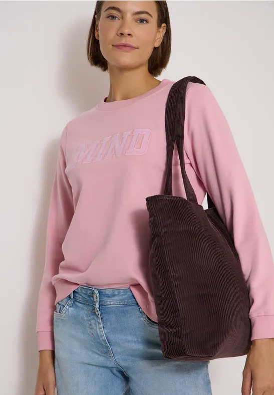 Femme en pull rose DKNY, jean bleu clair et grand sac épaule brun foncé.
