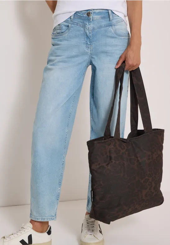 Persoon in lichtblauwe spijkerbroek en witte sneakers met een donker, gemêleerde tas.