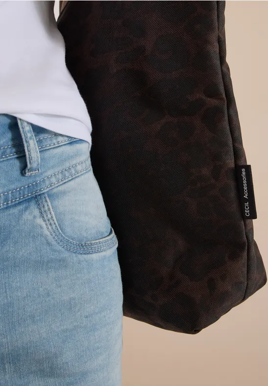 Close-up van persoon in jeans met een bruine tas met logo tegen neutrale achtergrond
