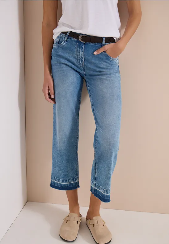 Person trägt hellblaue gerade geschnittene Jeans und beige Loafer vor neutralem Hintergrund.