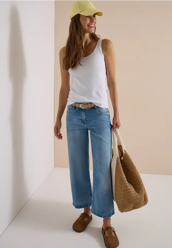 Frau in weißem Top, weitem Jeans, gelber Cap und Basttasche