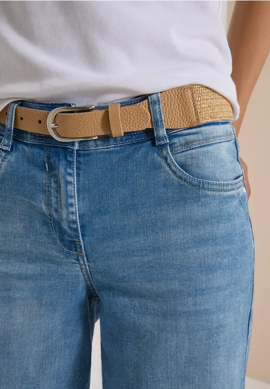 Nahaufnahme einer Jeanshose mit hellbraunem geflochtenem Gürtel, lockerer Sitz an der Taille.