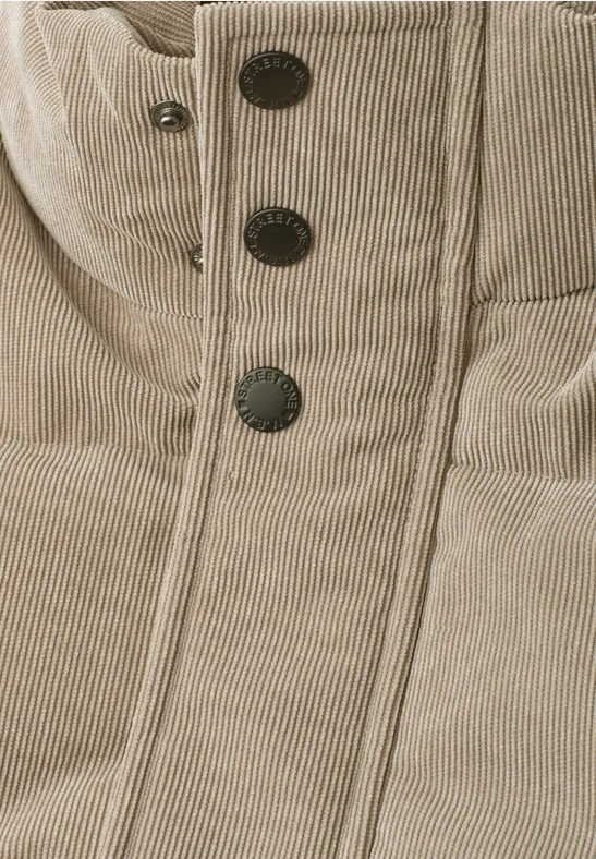 Nahaufnahme einer beigefarbenen gesteppten Jacke mit Kapuze und vier schwarzen Druckknöpfen.