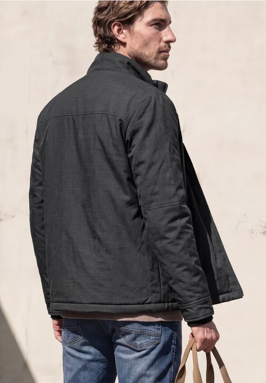 Ein Mann steht mit dem Rücken zur Kamera, trägt dunkle Jacke und Jeans, hält Schlüssel in der Hand.