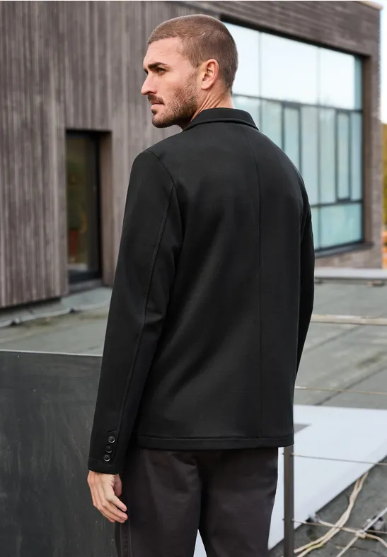 Een man op een dak gezien van achter, met een zwart jasje en donkere broek.