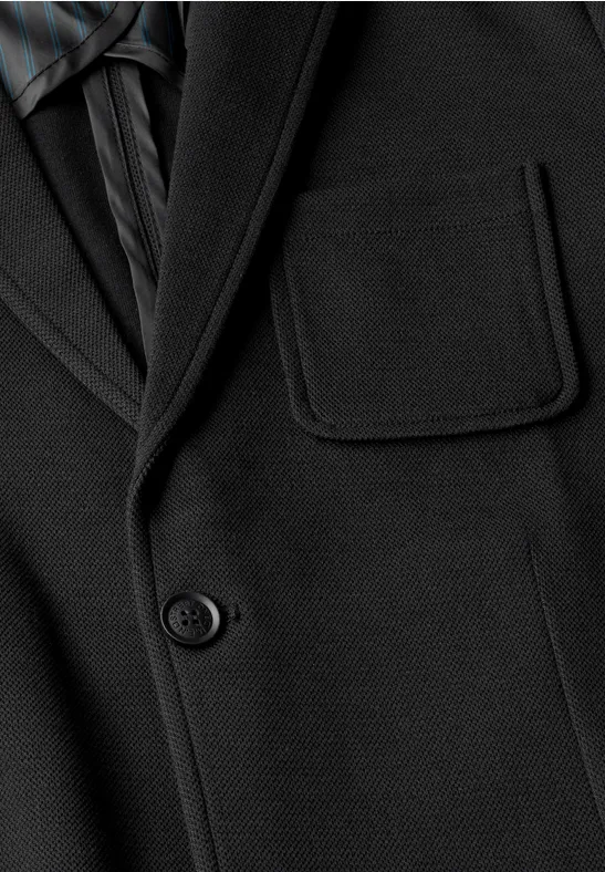 Close-up van een zwarte colbert met revers, borstzak en knoop, gecombineerd met een donker gestreept overhemd.