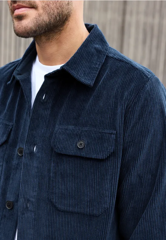 Een man draagt een donkerblauw corduroy jack over een wit T-shirt.