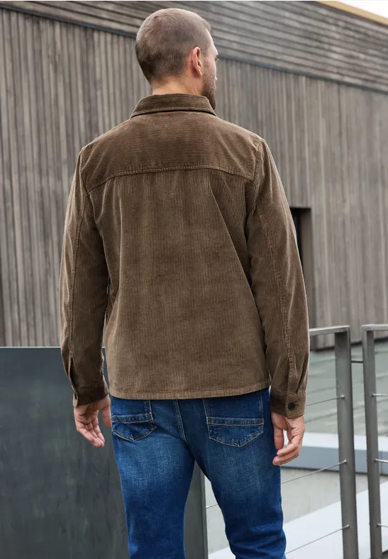 Man van achteren gezien in een bruine corduroy jas en blauwe jeans, op een modern dak.
