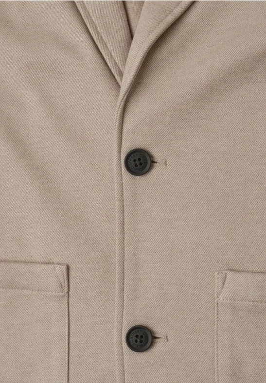 Close-up van een beige jas met twee zwarte knopen en opgestikte zakken.