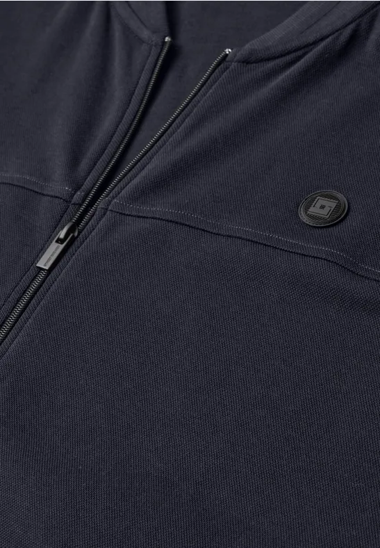 Detail van een donkerblauwe zip-up sweater met ronde logopatch op de borst.