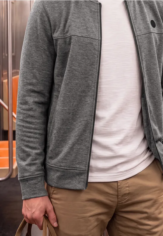 Persoon in grijs vest, wit T-shirt en beige broek staat in een metro.
