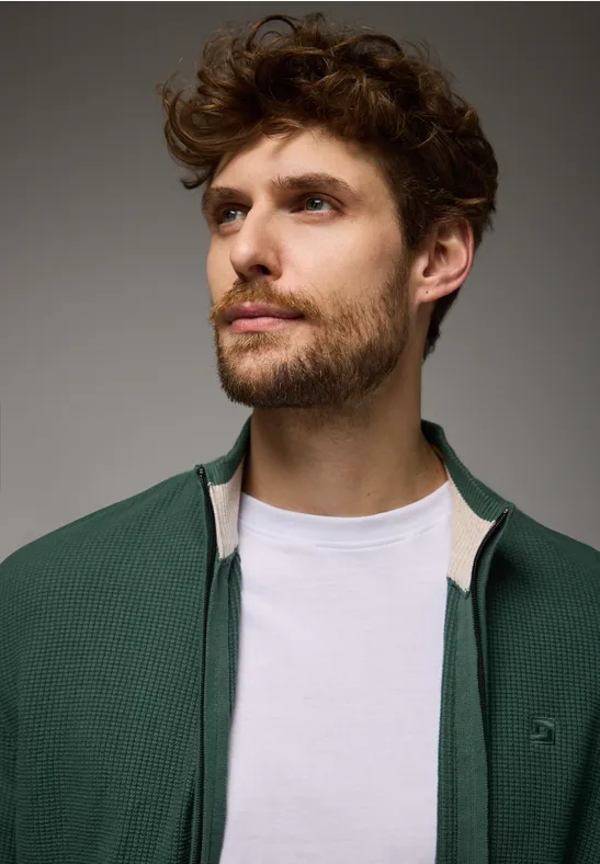 Jeune homme barbu en haut vert sur t-shirt blanc regarde à gauche.