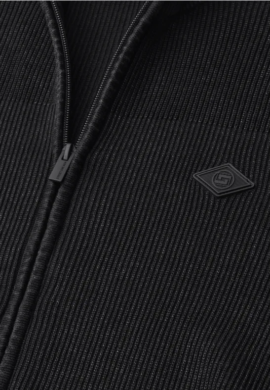 Nahaufnahme einer schwarzen Strickjacke mit Reißverschluss und kleiner Logo-Applikation.
