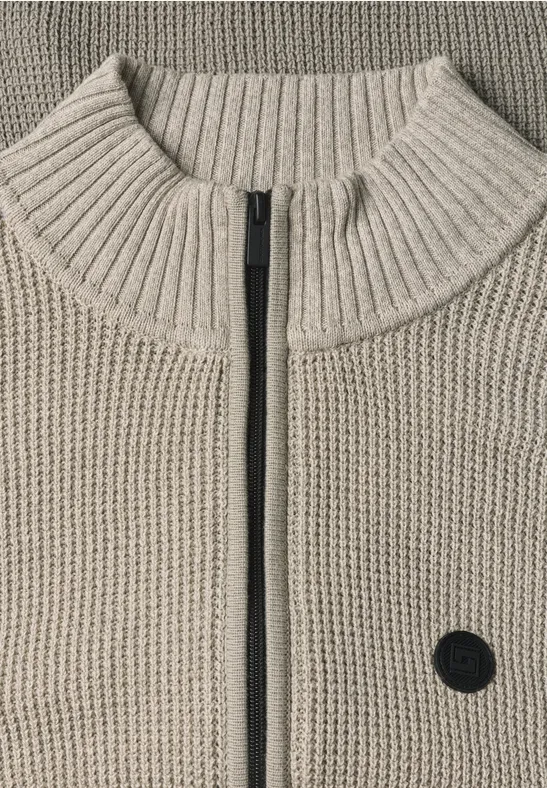 Beige gebreid vest met hoge kraag, centrale ritssluiting en klein zwart rond logo voorop.
