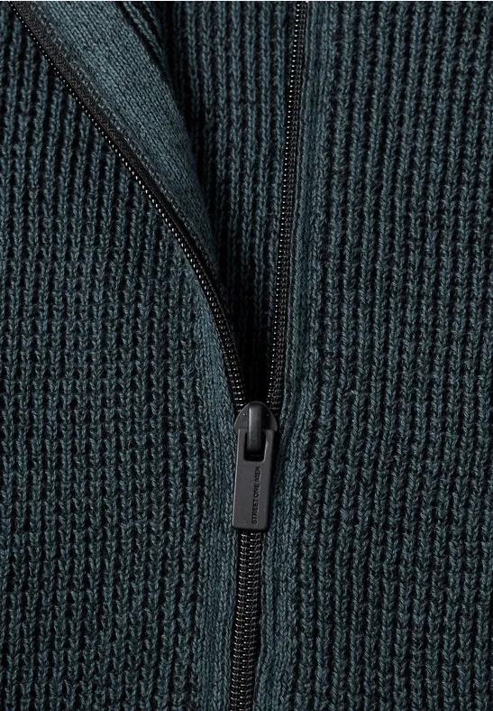 Nahaufnahme eines dunkelgrünen, gerippten Strickpullovers mit Reißverschluss.