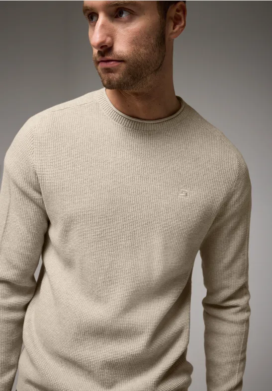 Mann in beigem Strickpullover schaut nach links.