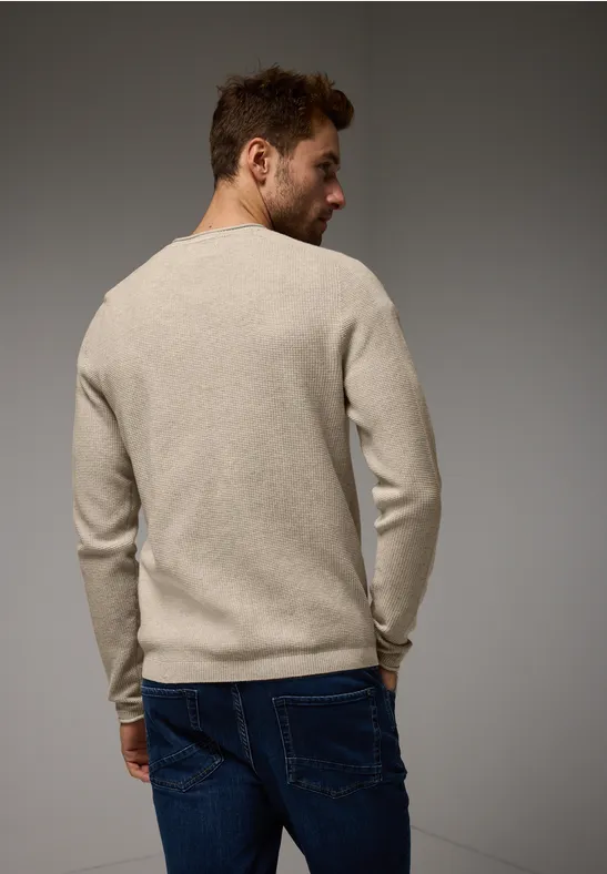 Ein Mann in beigem Pullover und Jeans steht mit dem Rücken zur Kamera.