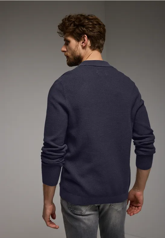 Man met baard, donkerblauwe trui en grijze spijkerbroek, van achteren te zien.