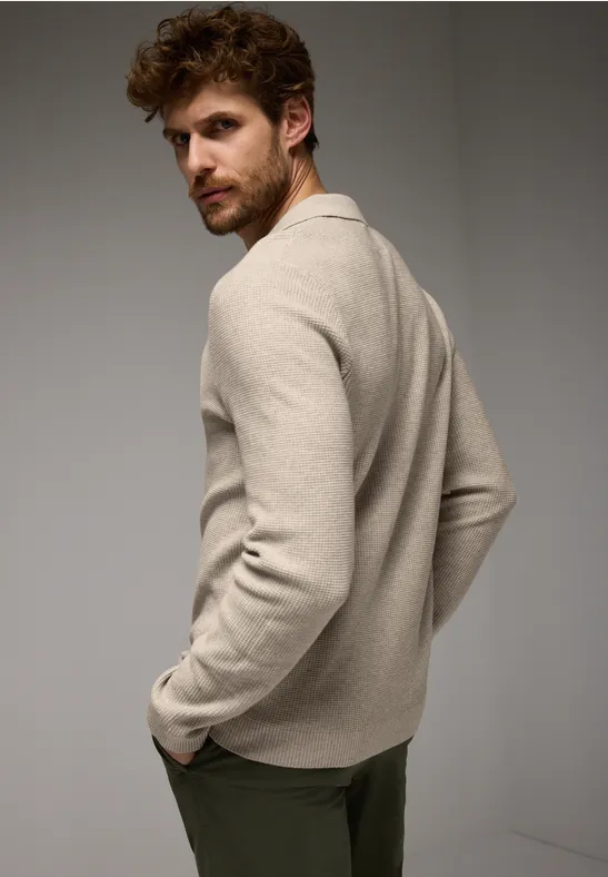 Mann mit braunem Haar trägt beigen Pullover und schaut über die Schulter.