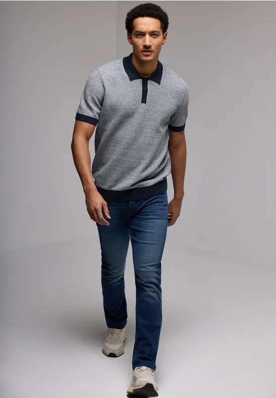 Mann in grauem Polo und Jeans läuft auf weißem Hintergrund.