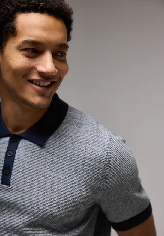 Mann mit lockigem Haar lächelt und trägt graues Poloshirt mit dunklem Kragen.