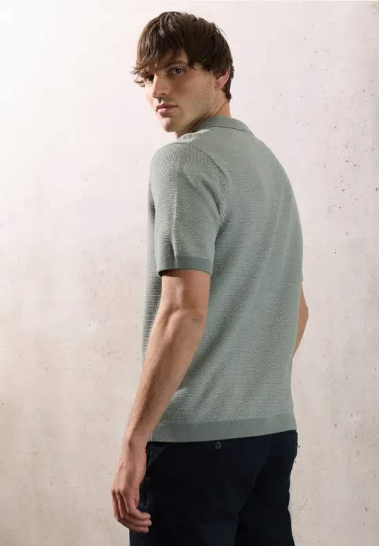 Een man in zijaanzicht draagt een lichtgroen T-shirt en donkere jeans, hij kijkt over zijn schouder.