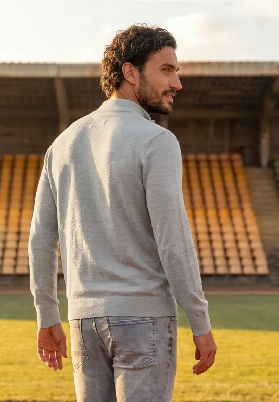 Ein Mann in grauem Pullover und Jeans steht auf dem Fußballfeld und blickt über die Schulter zurück.