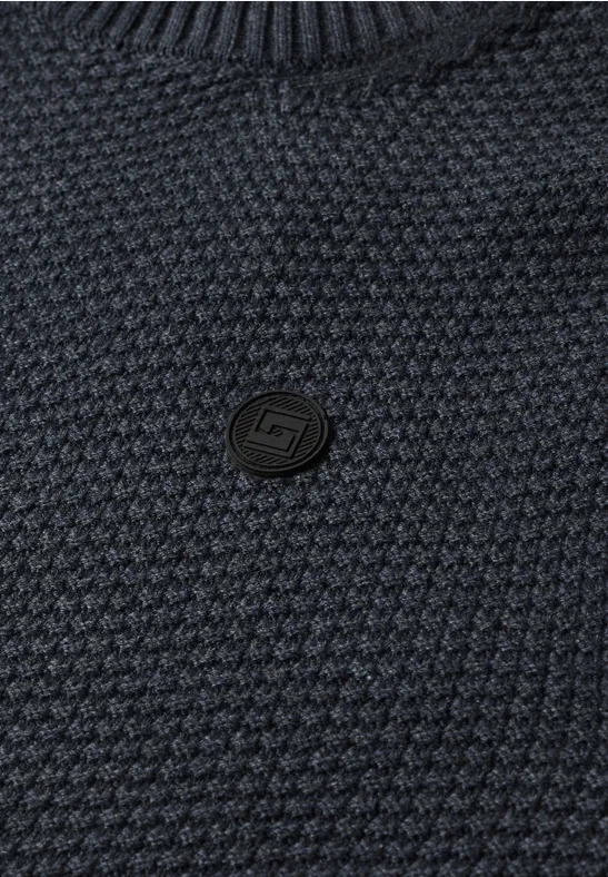 Close-up van een donkerblauw, gestructureerd gebreide trui met een ronde, zwarte logoknop in het midden.
