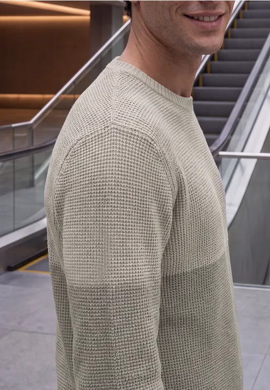 Een glimlachende man in een tweekleurige trui voor een roltrap in een moderne setting.
