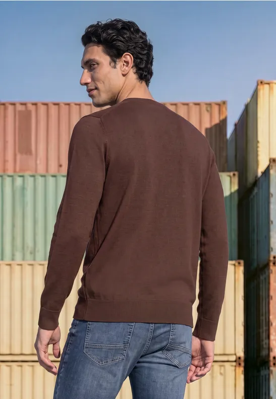 Ein Mann in braunem Pullover und Jeans steht vor bunten Containern, Blick nach oben.