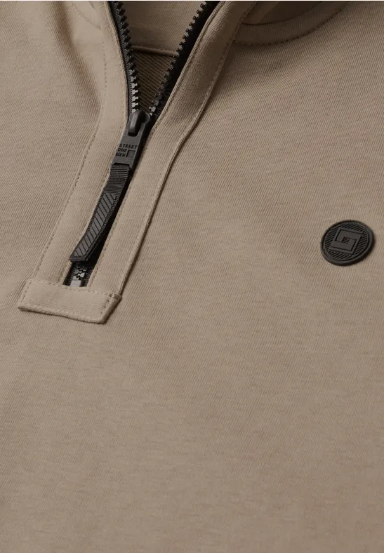 Nahaufnahme eines taupefarbenen Half-Zip-Sweatshirts mit schwarzem Reißverschluss und rundem Logo.