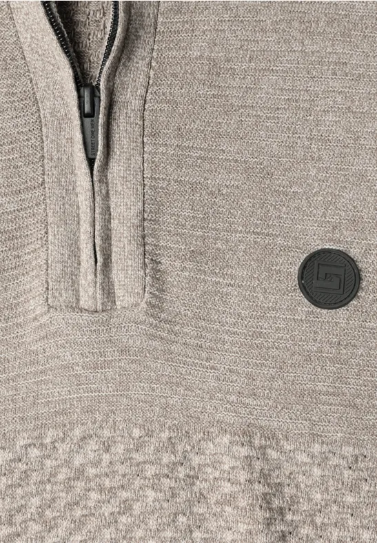 Gros plan d’un pull en maille beige avec fermeture éclair et écusson rond.