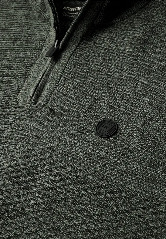 Nahaufnahme eines grauen Strickpullovers mit Reißverschluss und rundem Logo-Emblem