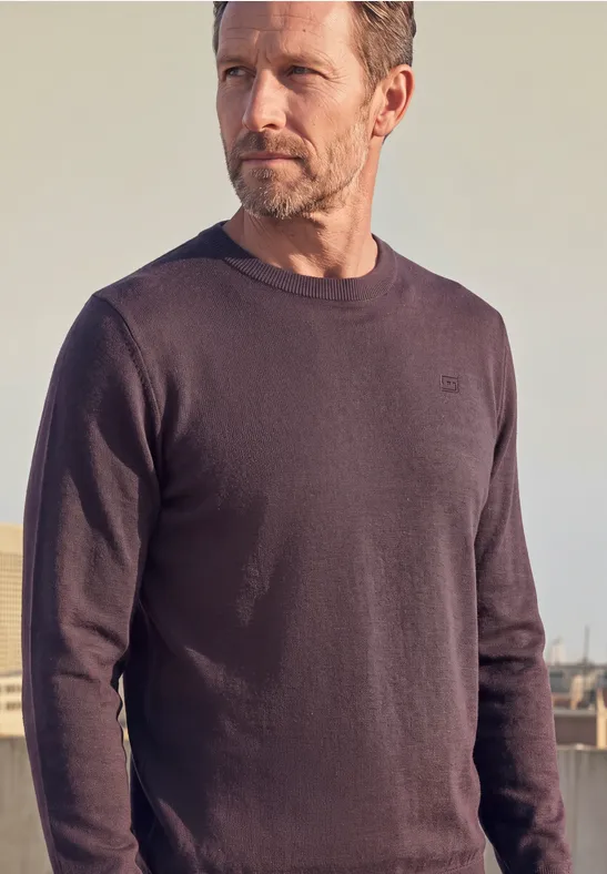 Homme portant un pull gris foncé devant un fond neutre.
