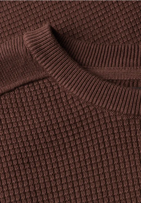 Nahaufnahme eines braunen, strukturierten Strickpullovers mit Waffelmuster.