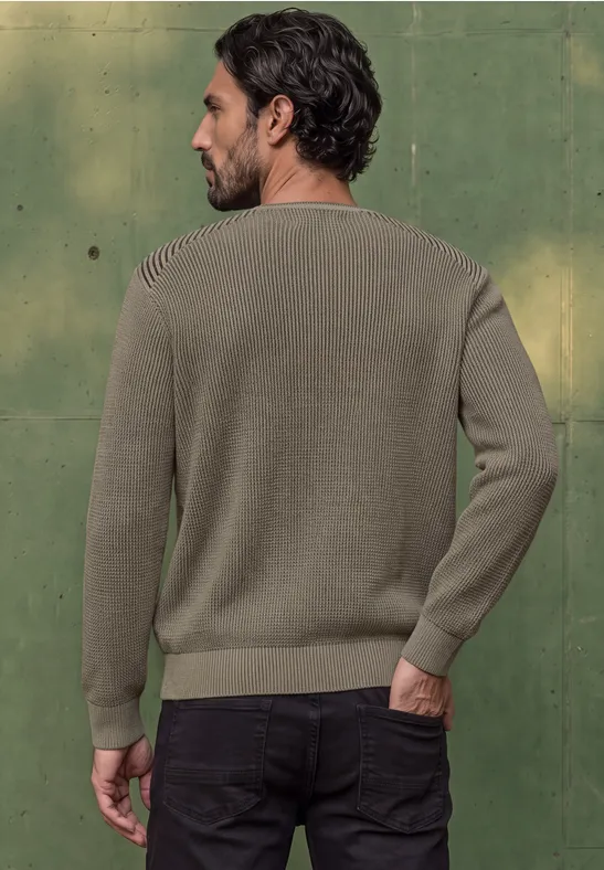 Un homme de dos en pull kaki devant un mur vert.