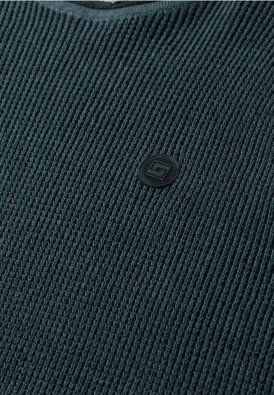 Nahaufnahme eines dunkelgrauen Strickpullovers mit V-Ausschnitt und kleinem Logo-Emblem auf der Brust.