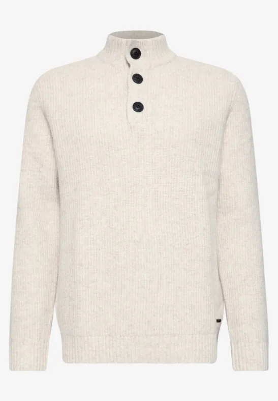 Pull en maille crème à col montant avec trois boutons noirs.