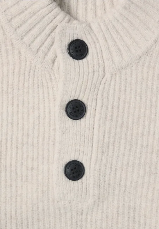Pull en maille beige côtelée avec col montant et patte de boutonnage ornée de trois boutons foncés.