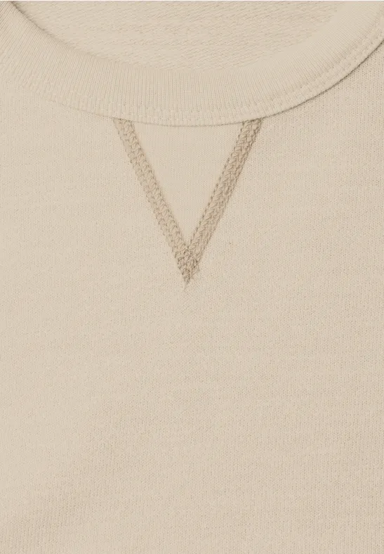 Nahaufnahme eines beigen Sweatshirt-Ausschnitts mit V-förmiger Ziernaht