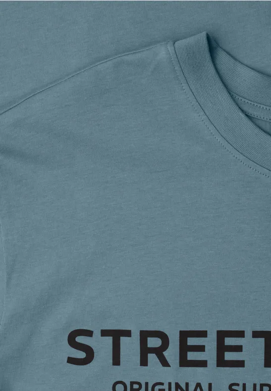 Gros plan d'un t-shirt bleu clair avec l'inscription noire 'STREET' sur l'épaule et le col.