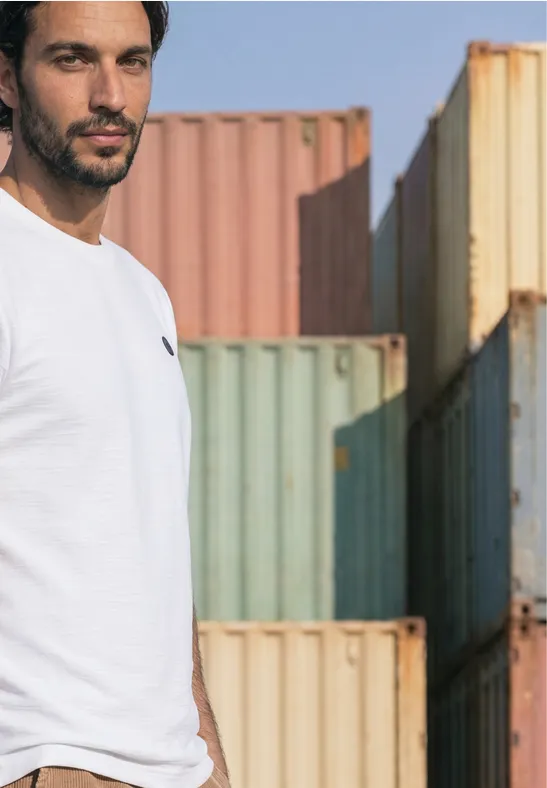 Een man in wit T-shirt staat voor kleurrijke zeecontainers.