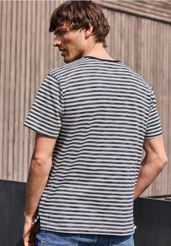 Ein Mann von hinten in gestreiftem T-Shirt vor einer Holzfassade.