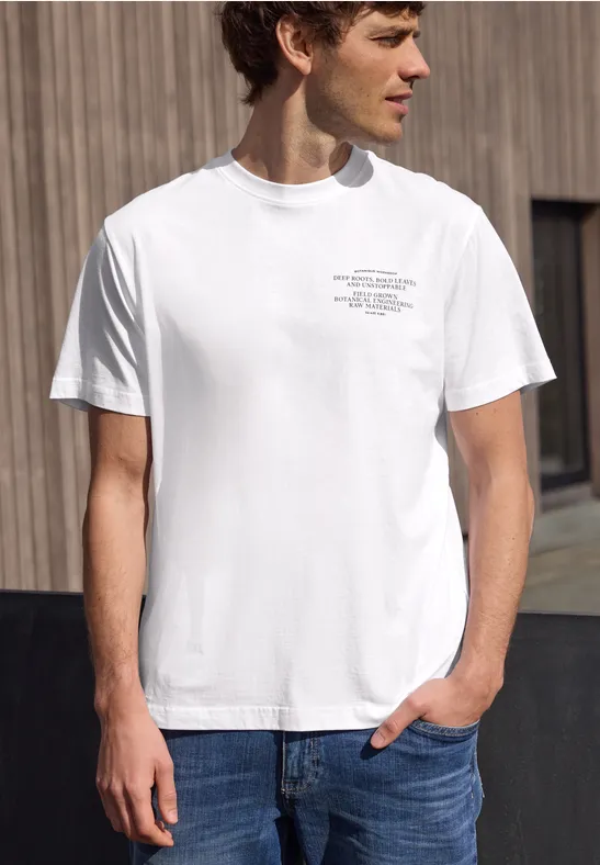 Mann in weißem T-Shirt und Jeans vor Holzwand.