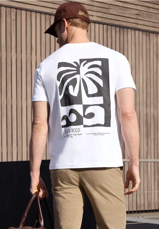 Mann trägt weiße T-Shirt mit Palme-und-Auto-Print, khakifarbene Hose, hält braune Tasche, steht vor Holzwand.